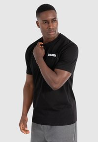 Sort bomulds T-shirt med et hvidt logo på brystet, korte ærmer og en klassisk pasform, parret med grå shorts.