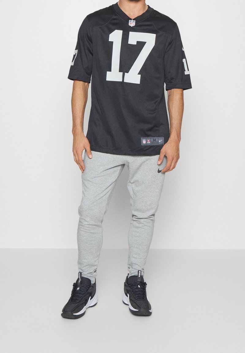 Person iført en sort NFL-trøje med nummer 17, lysegrå Nike sweatpants og sorte og hvide Nike sneakers, stående foran en ensfarvet baggrund.