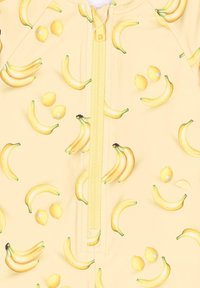 Geel zwemkostuum met een rits aan de voorkant, versierd met een patroon van bananen en citroenen. Glad textuur met levendige kleuren en speelse fruitgraphics.