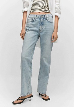 Persoon draagt lichtblauwe recht gesneden jeans, zwarte sandaalhakken, gestreept cropped topje en een los wit overhemd met opgerolde mouwen.