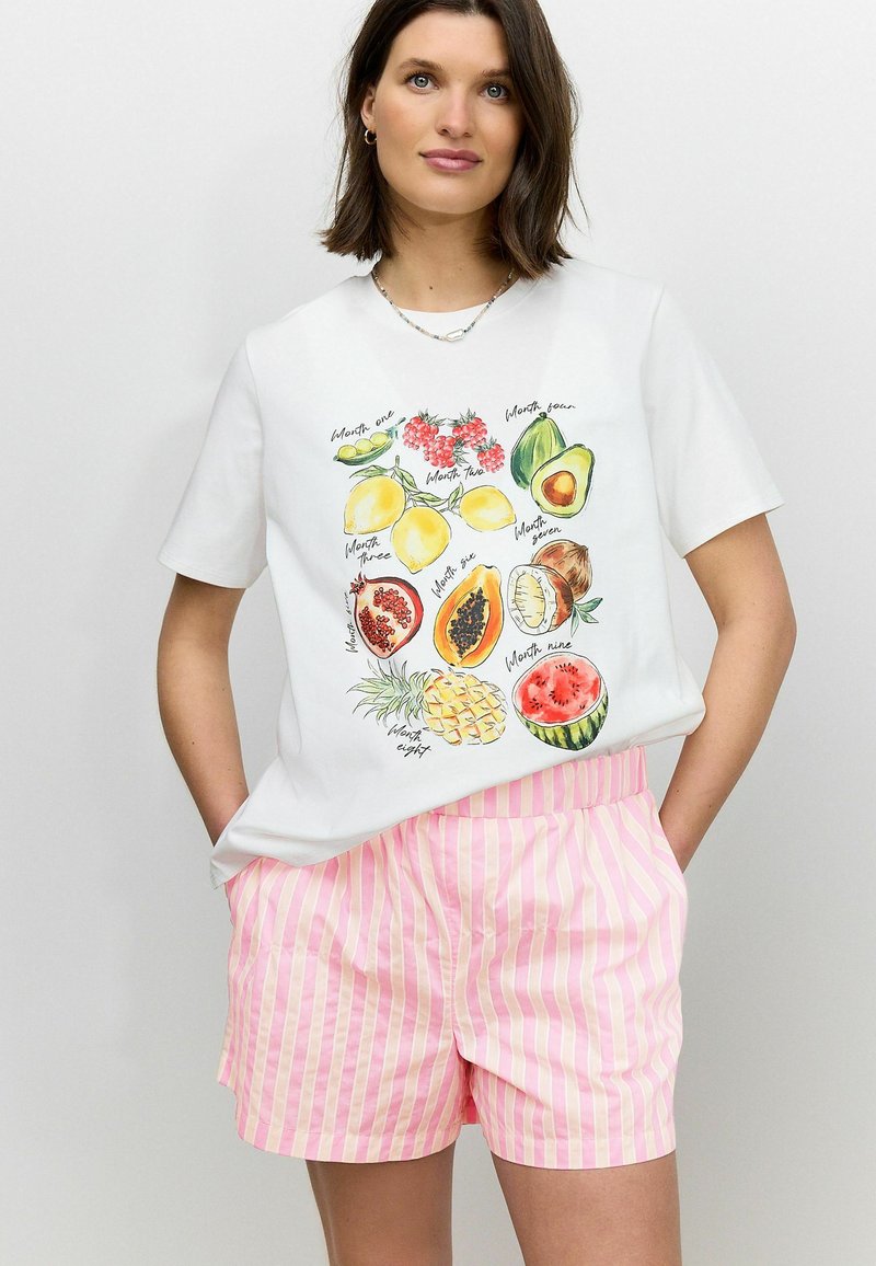 T-shirt en coton blanc avec des illustrations de fruits et du texte, associé à un short rayé rose. Le T-shirt a des manches courtes et une coupe décontractée.