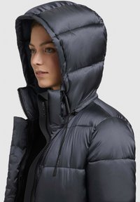 Chaqueta con capucha acolchada oscura y acabado brillante, que cuenta con un collar alto, cremallera frontal y ajustes con cordones.