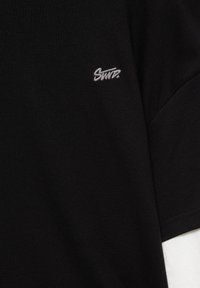 Chemise noire à manches courtes avec petit logo texte blanc brodé sur la poitrine gauche indiquant "SMTR."