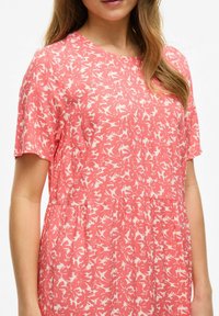 Robe corail à manches courtes avec un motif floral blanc, dotée d'un col rond et d'un détail de taille froncée, fabriquée en tissu doux.
