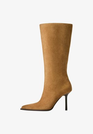 Knee-high suede boots in camel color with a pointed toe and a thin high heel. Smooth texture and sleek silhouette with minimal detailing.