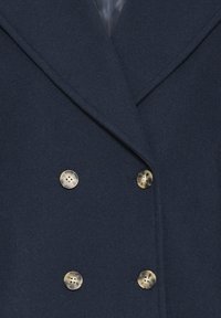 Navy zilā dubultā jāņa mēteli ar četriem gaiši brūniem marmora pogām un platām atlokiem.