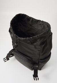 Black backpack with a textured zippered pocket, drawstring top, and adjustable straps. Made of smooth, durable fabric.