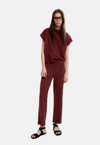 Bordowy dzianinowy top z krótkimi rękawami i pasującymi spodniami, oba o luźnym kroju i miękkiej fakturze. Połączone z czarnymi sandałami na ramiączkach.