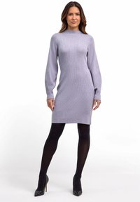 Helles lila geripptes Strickkleid mit langen Ärmeln, hohem Rundhalsauschnitt, figurbetontem Schnitt und knielanger Länge, kombiniert mit schwarzen Strumpfhosen und hohen Schuhen.