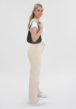 Pantalons évasés beiges à taille haute, associés à un t-shirt blanc ajusté. Un sac à main noir texturé est jeté sur une épaule. Baskets blanches.
