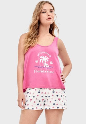 Frau trägt ein pinkfarbenes ärmelloses Oberteil mit der Aufschrift "South Beach Florida State" und einem Palmenmotiv, kombiniert mit weißen Shorts mit Palmen- und Muschelmustern.