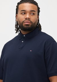 Marineblå polo i struktureret stof med klassisk krave, tre-knaps lukning og et lille logo på brystet.