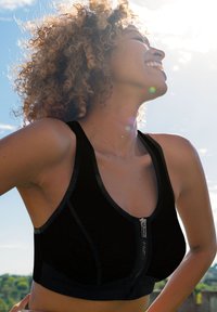 Black sports bra featuring a zip closure, adjustable straps, and a fitted design. Made from a textured material with seam accents.