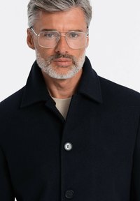 Cappotto di lana blu navy con un design elegante, caratterizzato da un ampio colletto, due bottoni e una texture liscia. Indossato sopra un top beige.