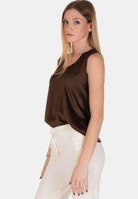 Top senza maniche in raso marrone con scollatura rotonda; abbinato a pantaloni bianchi a vita alta con zip frontale e taglio slim.