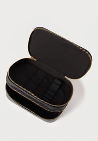 Μαύρη ορθογώνια θήκη με χρυστό φερμουάρ, ανοιχτή για να αποκαλυφθεί το μαύρο εσωτερικό με ιμάντα οργάνωσης. Λεπτή υφή εξωτερικά.