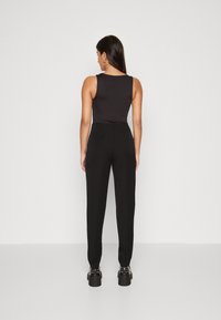 Combinaison noire sans manches avec un corsage ajusté et des jambes fuselées. Le matériau semble lisse avec des détails de design minimaux. Les chaussures ont des semelles épaisses.