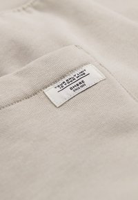 Tela beige claro con una pequeña etiqueta blanca cosida que dice "TU ÚNICO LÍMITE ES TU MENTE" y "OMBRE desde 1995."