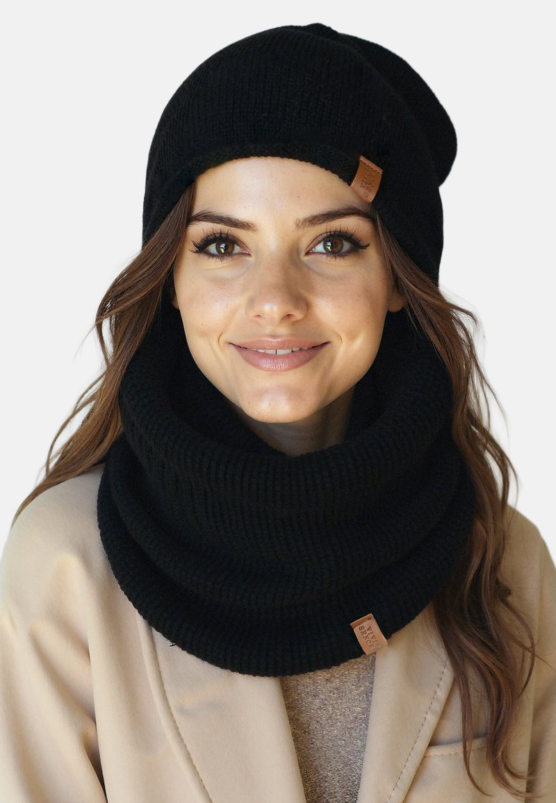 Conjunto de gorro de punto negro y bufanda infinity, con textura acanalada y una pequeña etiqueta de cuero. Material cálido y suave con un ajuste ceñido.