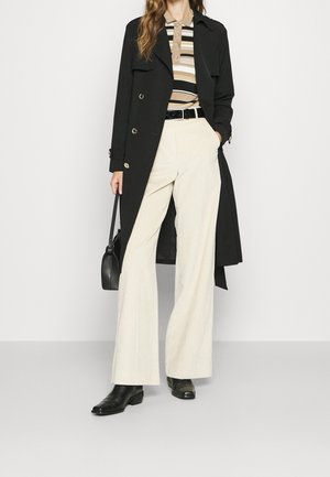 Musta kaksirivinen trenssitakki; beige raidallinen poolopaita; kermaiset leveälahkeiset samettihousut; musta käsilaukku; mustat nilkkurit.