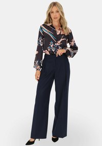 Czarna bluzka w kwiatowy wzór z niebieskimi i różowymi akcentami, zestawiona z granatowymi spodniami o wysokim stanie. Gładki materiał, dopasowany krój i czarne szpilki.