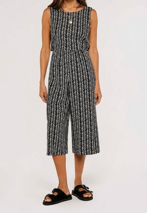 Schwarz-weiß gemusterter Jumpsuit im Fischgrätmuster mit ärmellosem Design, elastischem Bund und gekürzten Beinen, kombiniert mit schwarzen Sandalen.