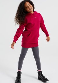 Rdeča kapuca s kenguru žepom, v kombinaciji z sivi športnimi pajkicami. Črne čevlje z vezalkami z rožnatimi in belimi črtami dopolnjujejo obleko.