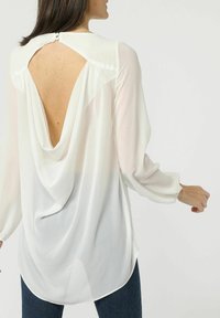 Blusa blanca con mangas largas y transparentes, y escote profundo en la espalda. Diseño drapeado con dobladillo redondeado y cierre de botón en la parte trasera.
