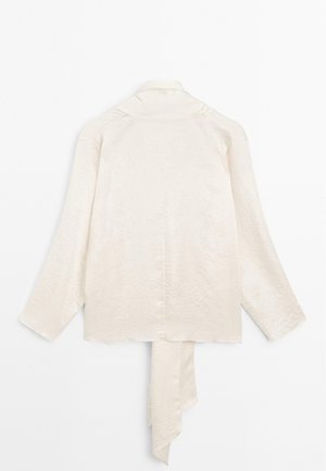 Chemise à manches longues couleur crème en tissu lisse avec une finition légèrement texturée ; elle présente un détail de lien drapé au dos et un col.