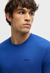 Blue textured knit sweater featuring a round neckline and a subtle black "BOSS" logo on the chest. Close-up view of the garment.