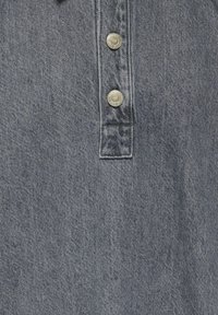 Siva denimska tkanina z dvema kovinskima gumboma, ki sta vertikalno poravnana na šivanem zapahu, ki prikazuje teksturo in šive v podrobnostih.