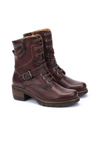 Brown leather ankle boots with a rounded toe, lace-up front, side buckle strap, and textured rubber sole. Features stitched detailing.