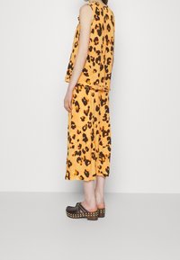 Leopard print two-piece outfit featuring an orange top with a relaxed fit and a matching skirt. Brown clogs with gold studs complement the look.