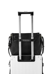 Borsa a mano in pelle nera con finitura testurizzata, posata su una valigia rigida bianca con manico estraibile.