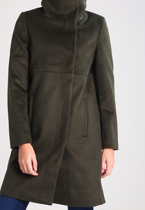 Manteau vert foncé longueur genou avec col haut et fermeture avant dissimulée, porté par une personne les mains détendues le long du corps sur un fond uni.