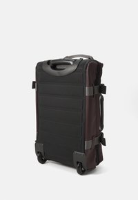 Black and dark burgundy wheeled suitcase with a textured surface, sturdy handle, side straps, and reinforced corners for durability.