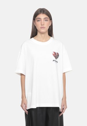 T-shirt bianco in cotone con design di un cuore rosso glitterato e un logo. Vestibilità ampia con maniche corte e scollatura rotonda.