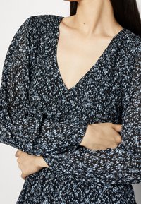 Robe noire à motifs floraux bleus clairs, décolleté en V et manches longues. Présente une texture plissée et une taille élastique pour un ajustement parfait.