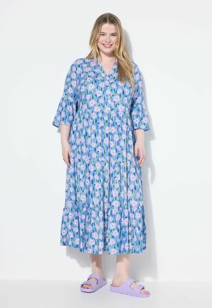 Abito maxi con motivo floreale in blu, con maniche corte a campana e design a strati. Abbinato a sandali scivolati di colore viola chiaro.