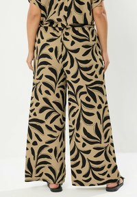 Vidbyxlade byxor i en beige tyg med ett mönster av svarta blad och prickar. Har en elastisk midja och platta sömmar.