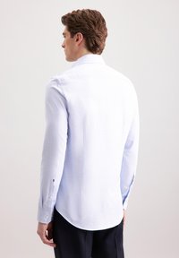 Camicia a maniche lunghe azzurro chiaro con una texture liscia, polsini abbottonati e orlo curvo. Presenta un colletto classico e dettagli di cucitura sottili.