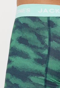 Camo-gedruckte Shorts mit einem hexagonalen Muster in Grün und Marineblau, mit einem hellblauen elastischen Bund, der mit "JACK & JONES" beschriftet ist.