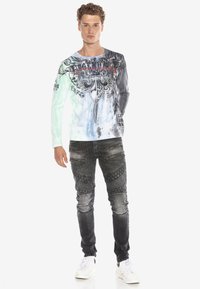 Langærmet, flerfarvet skjorte med grafiske designs og tekst. Kombineret med mørke, teksturerede jeans, prydet med lynlåsdetaljer. Hvide sneakers.