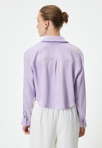 Lilla, cropped silke bluse med en rygfold, lange ærmer og knapmanchetter. Glat tekstur, klassisk krave og enkelt design.