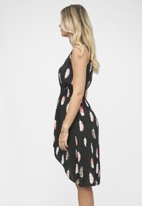 Czarna sukienka z wzorem piór w kolorach różowym, beżowym i białym. Sukienka ma dopasowaną talię i luźną, lekko opadającą spódnicę.