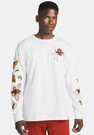 Witte blouse met lange mouwen met kleurrijke insectillustraties op beide mouwen en een spinnenafbeelding op de voorkant. Katoenen materiaal, relaxte pasvorm.