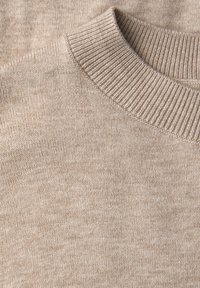 Beige neulottu pusero, jossa on resorikuvioitu pyöreä kaulus. Pehmeä rakenne ja tasaiset ompeleet, jotka esittelevät hillityn harmaaruskean kuvion.