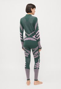 Grønn termoutfit som består av en mønstrete langermet topp og tettsittende leggings med rosa geometriske detaljer. Strikket tekstur og kroppsnær design.