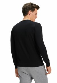 Schwarzer, langärmeliger Pullover aus Strickmaterial mit schlichter Gestaltung und gerippten Bündchen, getragen über grauen Freizeit-Hosen, von hinten gezeigt.