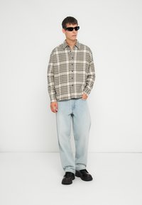 Ruudullinen paita beige- ja mustavalkoisena, napitettava ja rento malli; yhdistettynä vaaleansinihin löysiin farkkuihin ja mustiin chunky-tennareihin.